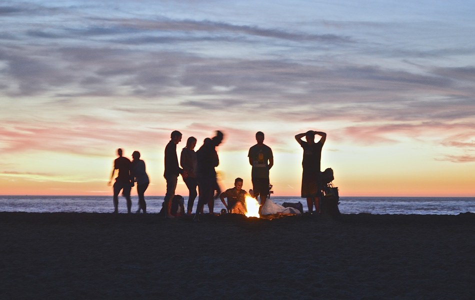 group of people on the beach around a fire at sunset